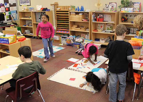 Children working on different activities while being spread out in the classroom.