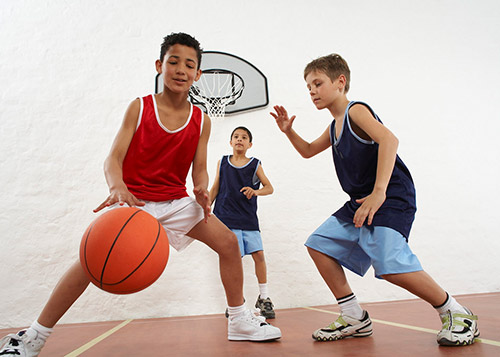 Three boys play basketball in an indoor basketball stadium.