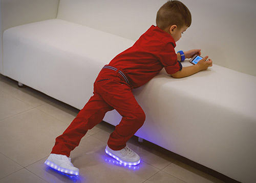 A boy wearing LED shoes playing on a phone.