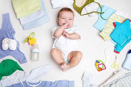 Baby lying on its back surrounded by baby clothes