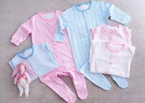 Pink and blue baby clothing sets with a tiny pink baby toy next to them