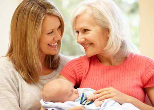 Mother and daughter smiling at each other while holding the baby