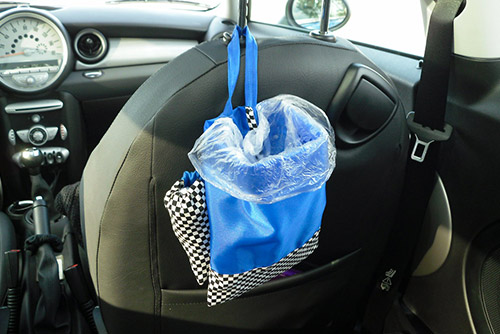 A blue trash bag hung from the backseat of a car.