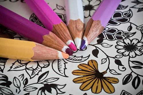 A yellow, fuschia, pink, white, and lilac coloured pencil places on a colouring book