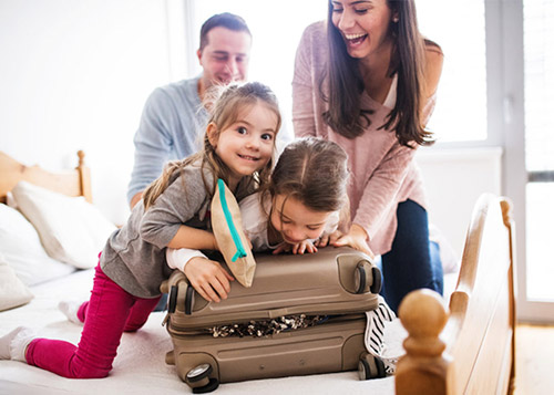 Daughters helping mom close a stuffed suitcase while dad laughs. Packing right for a holiday is a fun activity.