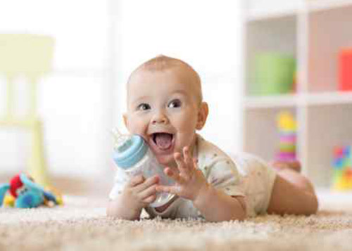 Baby holding a feeding bottle and smiling while lying down on its stomach