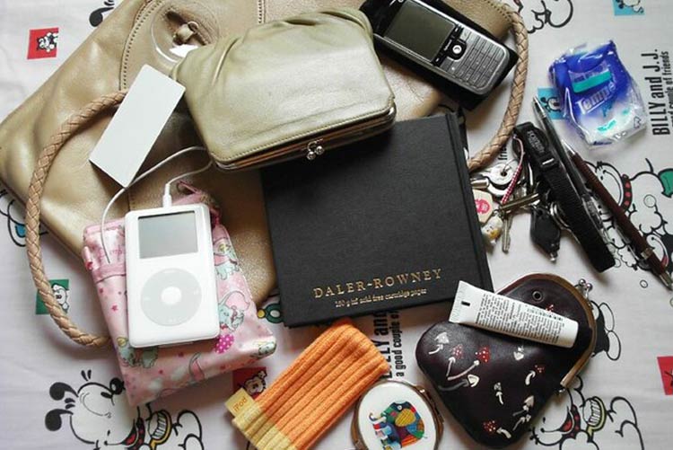 Contents of a handbag such as mobile, lip balm, wallet., keys, music player, and other thing scattered around the bag