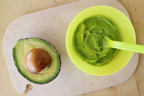 An avocado and a bowl of avocado mash on a chopping board