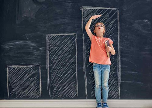 A young girl measuring her height using bars drawn on a blackboard