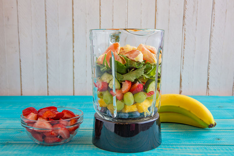 Blender filled with grapes, berries, bananas, and kale leaves!