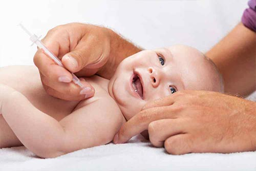 A smiling infant being immunised with a syringe by an adult