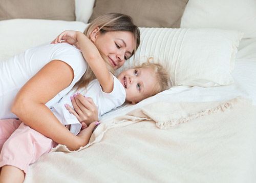 Mother and young daughter smiling and hugging on the bed