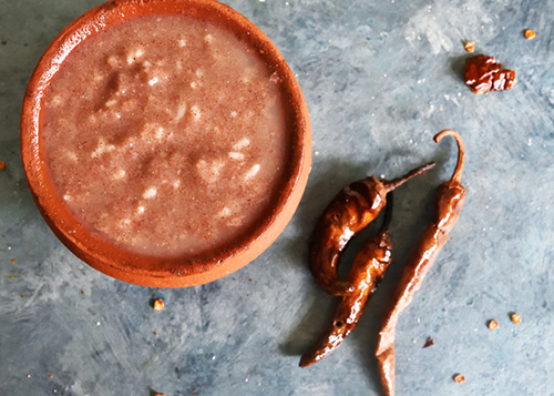 A bowl of ragi porridge set on a stone table with red chillies on the side