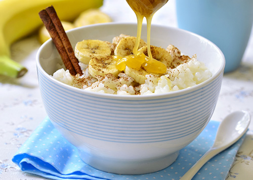 A bowl of banana rice topped with cinnamon and honey served with chopsticks