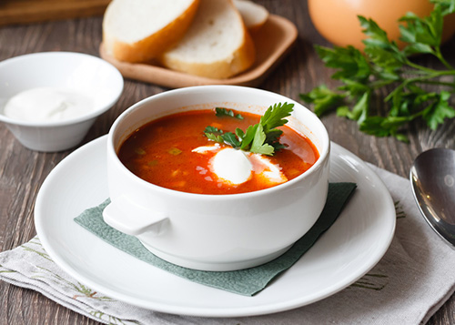 A bowl of tomato soup with fresh cream, garlic bread, and fresh greens