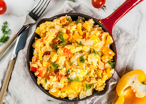 Scrambled eggs in a pan with tomatoes and bell paper on the side