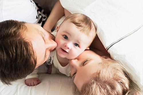 A mother and father kissing their cute baby on each cheek