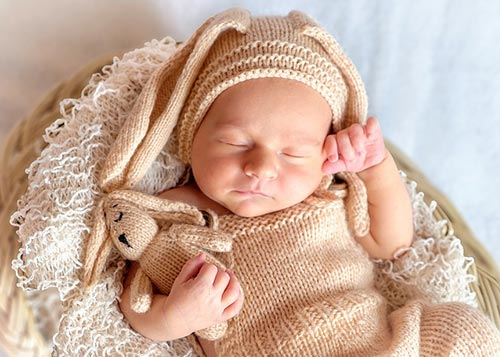 Cute infant in woolen clothing taking a nap in a basket