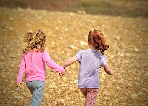 Two young girls holding hands and walking