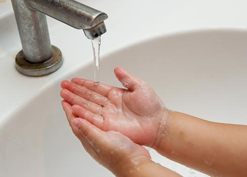 Young baby washing his hands with soap under a faucet