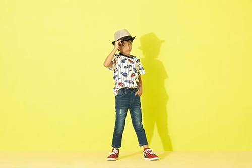 Young boy in jeans and patterned t-shirt holding his hat