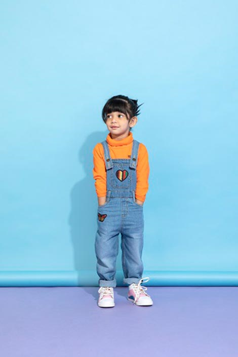 Cute young girl in Denim dungarees and orange full-sleeved turtleneck