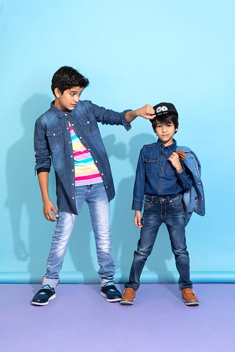Two young kids wearing denim shirts and jackets with the older one pulling on the younger one’s hat