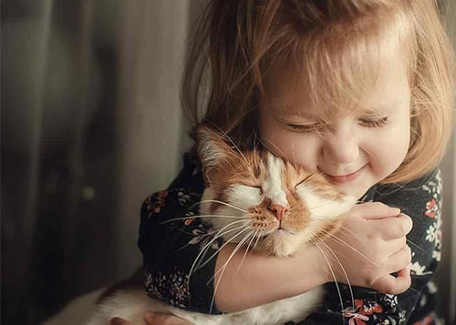 A cute blonde baby girl hugging a ginger cat lovingly