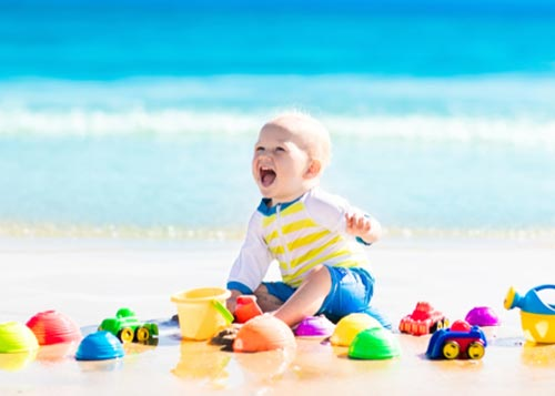 Adorable young boy sitting and playing with toys on a beach!