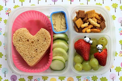 A kids lunch box with a sandwich, cucumber, fruits, and biscuits.
