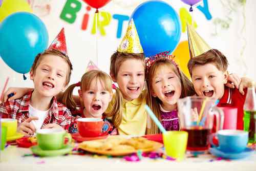 Birthday boy and his friends standing around a table with food cheering with birthday decorations in the background.