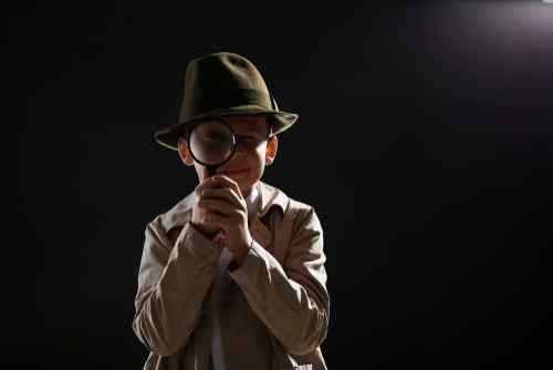 Little boy in detective attire looking through a magnifying glass