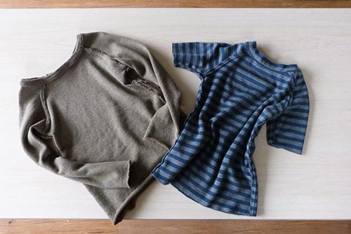 A grey thermal t-shirt and a striped blue t-shirt placed on a plain white background on a wooden desk