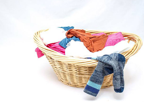 A wicker laundry basket filled with clothes with a pair of socks hanging off the edge