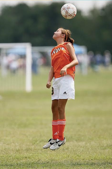 Girl playing soccer. Heading the ball.