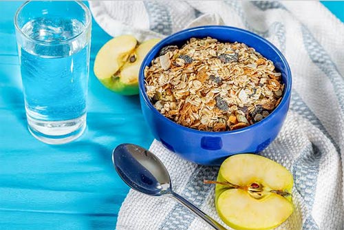 A bowl of muesli, apples, and a glass of water