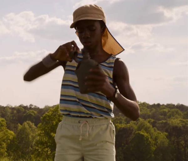 Lucas wearing a sleeveless t-shirt, shorts, and cap looking inside a water bottle.