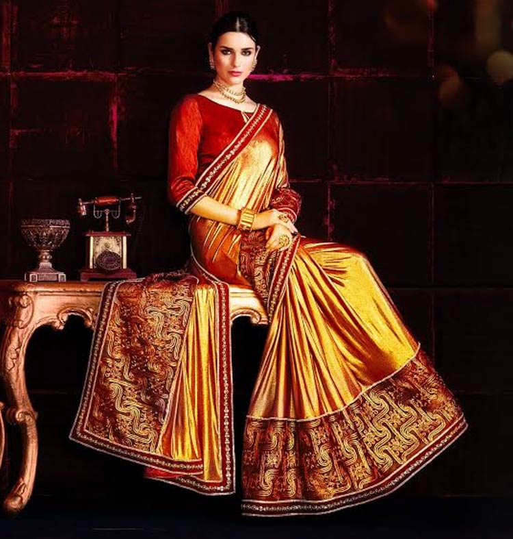 A woman in a gold-coloured sari sitting on a desk