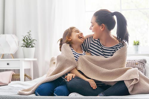 Mother and daughter smiling at each other with a shawl wrapped around them.