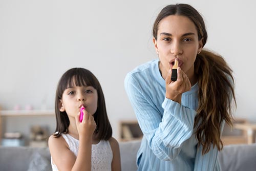 Daughter imitating mom putting on lipstick.