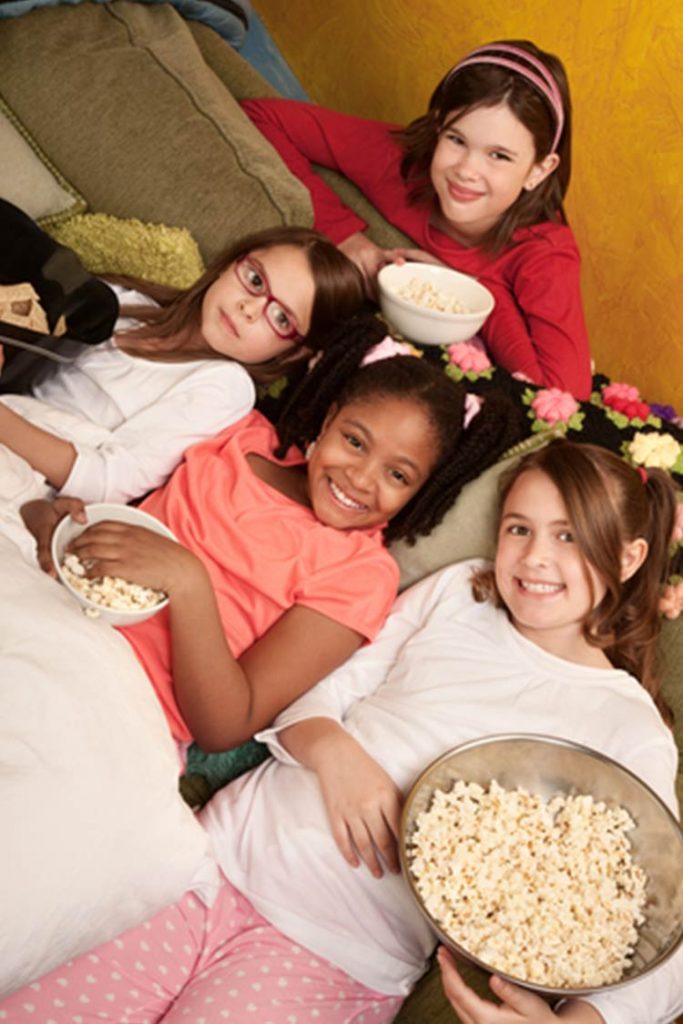Girls sitting on the couch in their pyjamas with bowls of popcorn