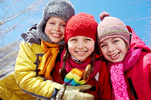 Three kids dressed in colourful layers of winter clothing and smiling.