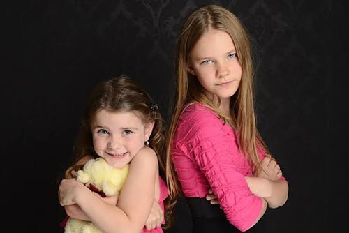 Two girls about 2 years apart in age standing with their backs against each other