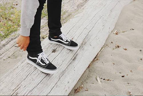 Boy adjusting the hem of his jeans while wearing black sneakers. Summer fashion.