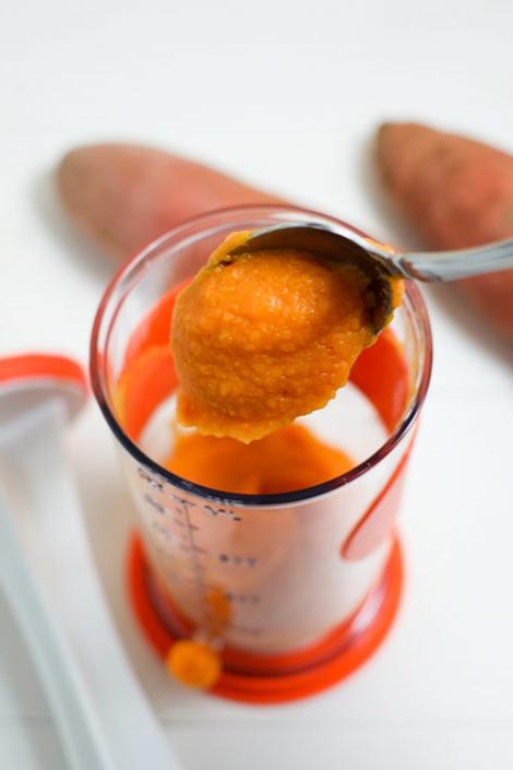 A spoon scooping sweet potato mash from a glass
