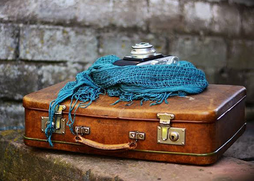 A closed compact brown suitcase with a blue shawl and camera on top. Classic packing style - light and stylish.