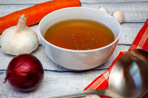 Picture of veggie broth in a bowl with a carrot, onion, and cloves of garlic around it