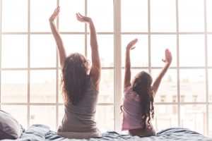 Mother and daughter stretching on bed in the morning