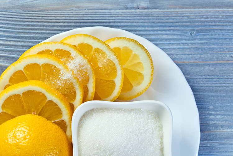 A bowl of sugar and lemon slices placed on a plate.