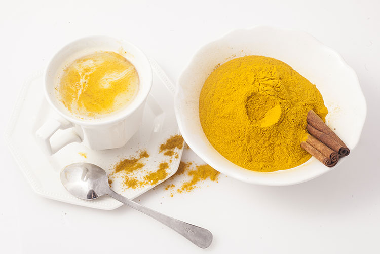 A bowl of turmeric powder and a glass of milk placed next to each other.